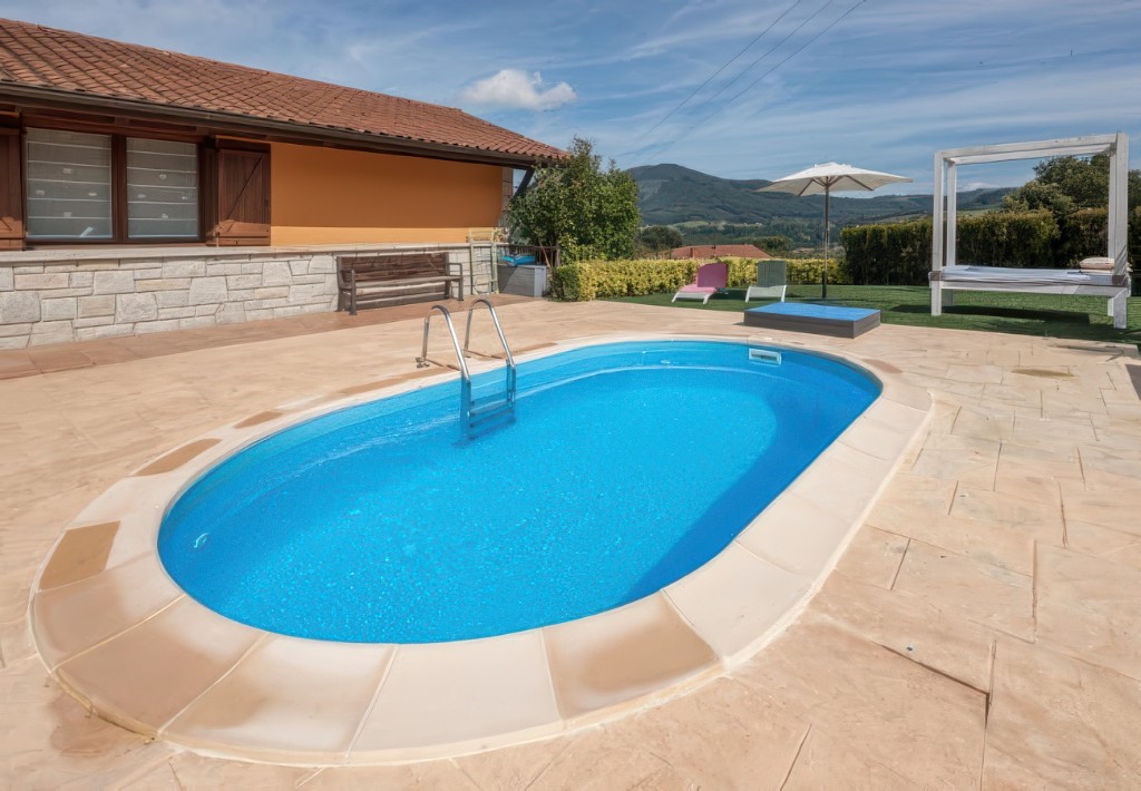 Oval pool with beige coping beside a rural house, starting photo for Mix&Design add pool accessories
