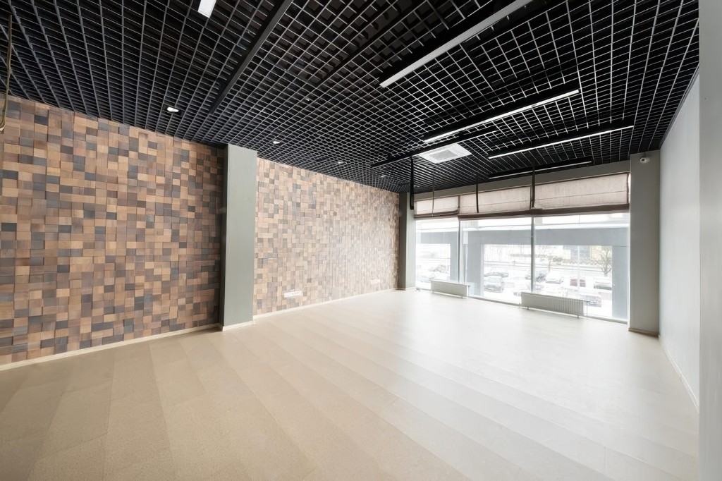 Empty shop with a light tile floor, a wood-tessera wall and a grid ceiling, starting photo for Mix&Design microcement